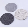 Three round grey cotton cord coasters arranged on a wooden table.