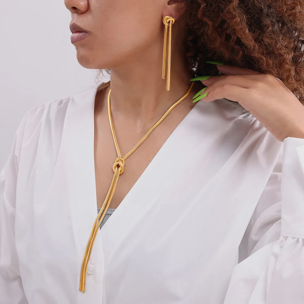 Gold colour titanium steel necklace with knotted tassel pendant and matching earrings on a white background.