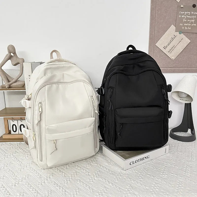 Large capacity nylon schoolbag in black or white, 20-35L, with curved shoulder straps and solid colour design.