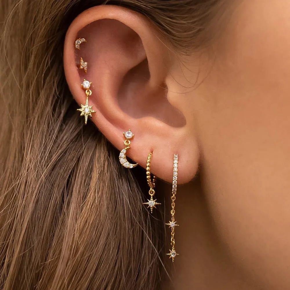 Set of six gold electroplated earrings with zircon studs and chain tassels on a flat surface.
