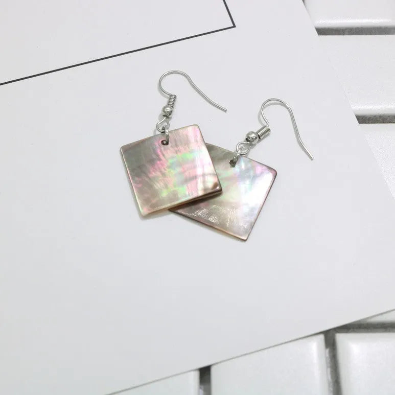 Handmade women's shell earrings in rectangular and square geometric shapes on a neutral background.