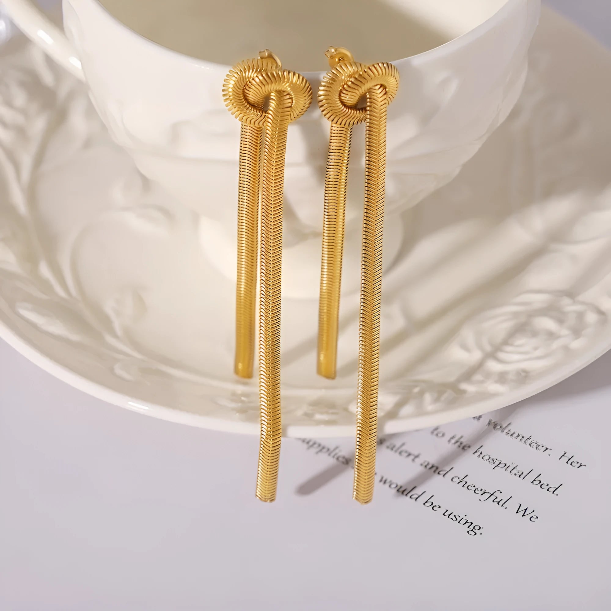 Gold colour titanium steel necklace with knotted tassel pendant and matching earrings on a white background.