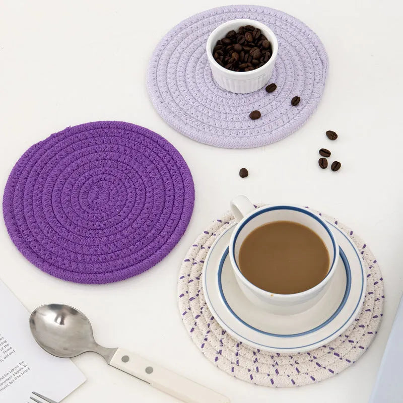 Three round grey cotton cord coasters arranged on a wooden table.