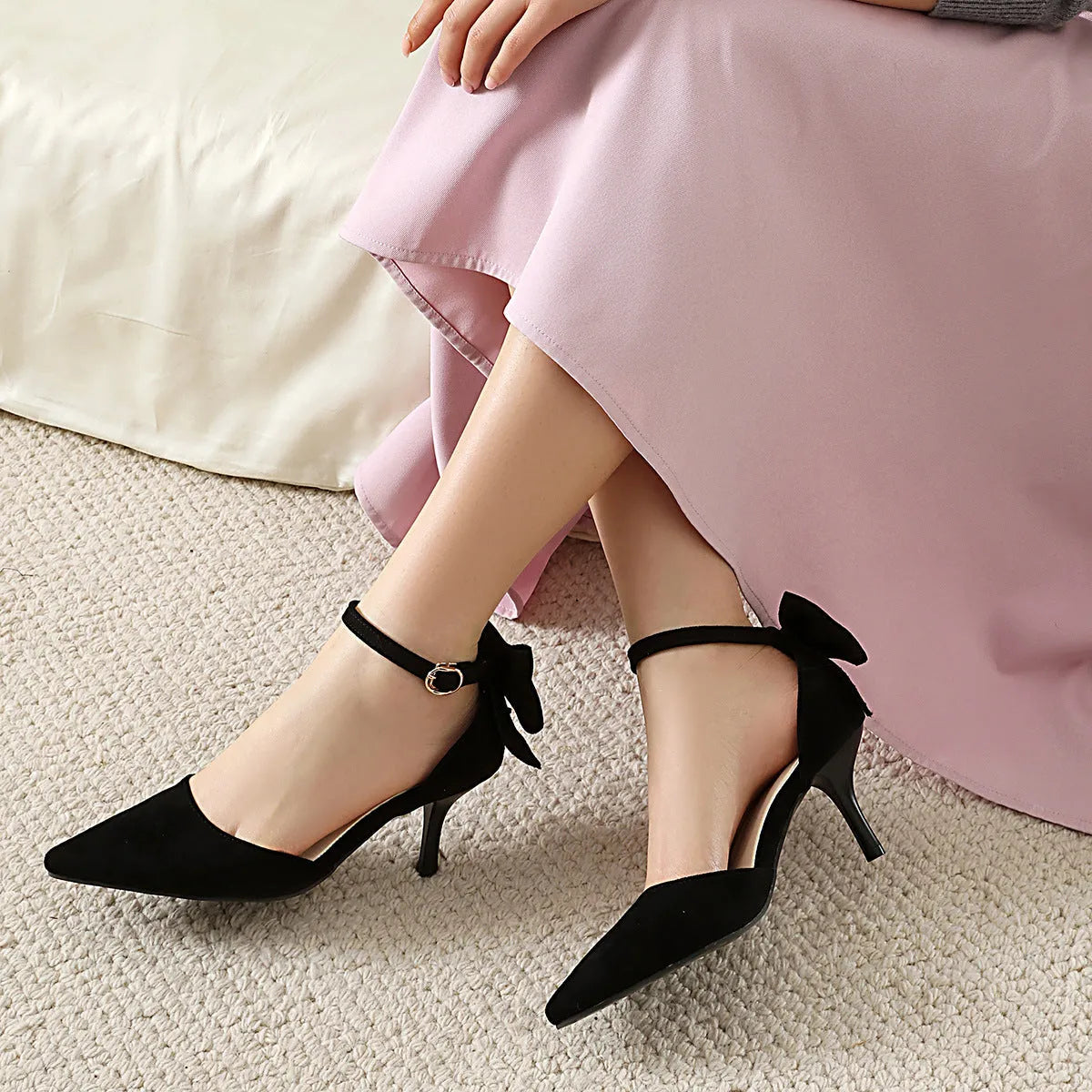 Women's black suede stiletto heels with pointed toe, bowknot detail, and buckle fastening on rubber sole.