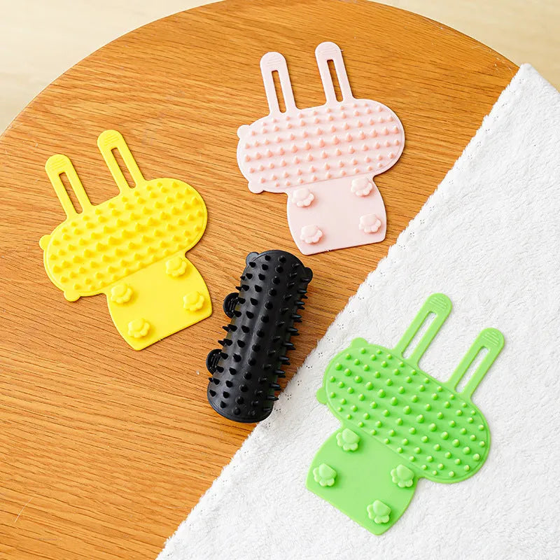 Silicone cat grooming comb with adjustable strap mounted on a table leg, shown in yellow.