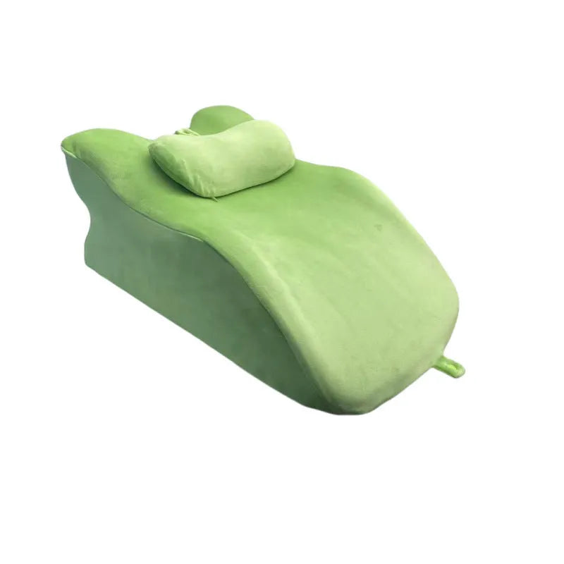 A flat stomach sleeper pillow shown on a bed, designed for prone sleeping and reading.