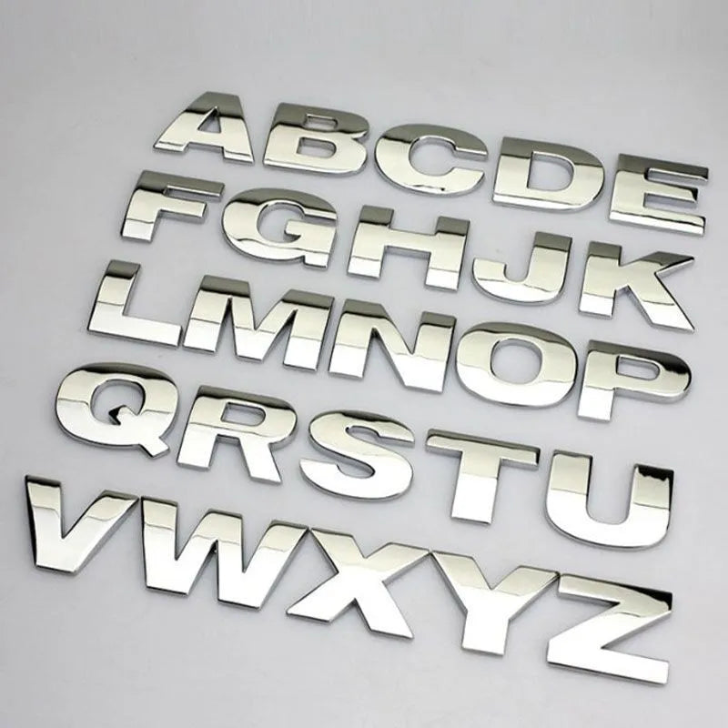 3D metal car letter sticker in zinc alloy, shown in black and silver finishes, approx. 2.5 cm in size.