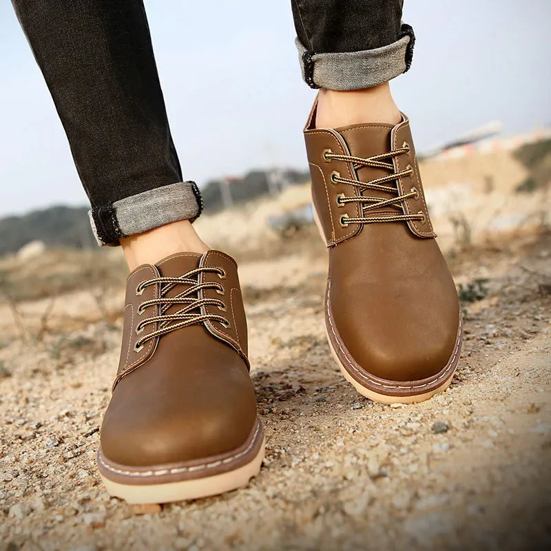 Men's black mid-top leather work boots with a flat rubber sole, shown from the side.