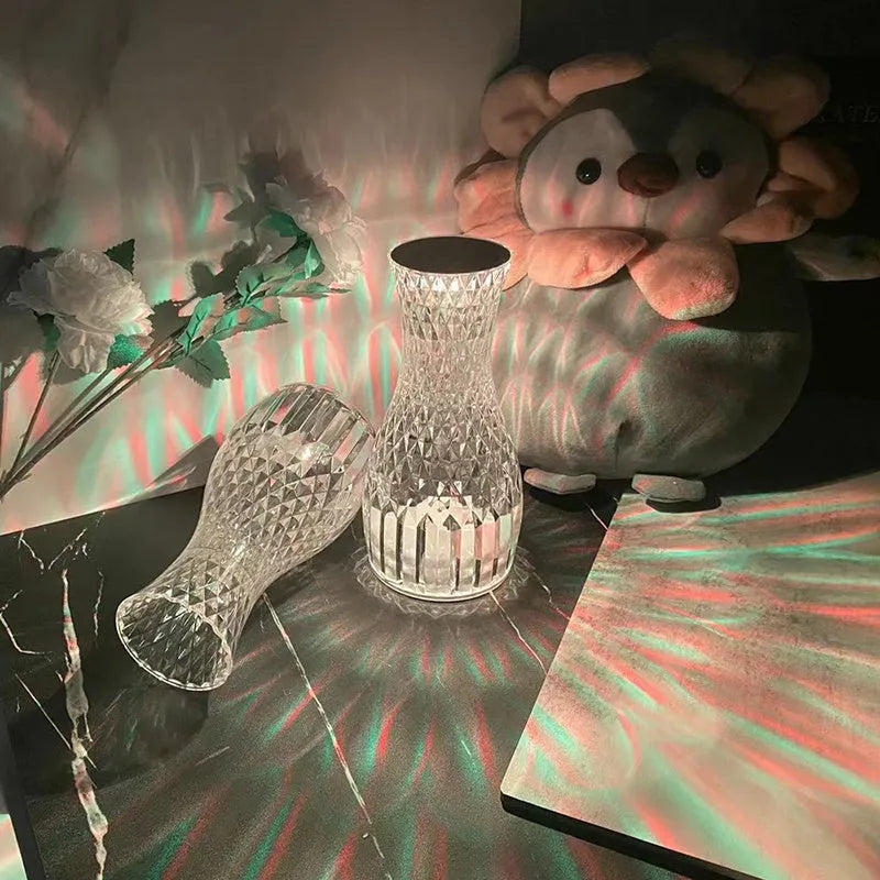 Transparent crystal vase shaped LED table lamp with remote control on a wooden bedside table.