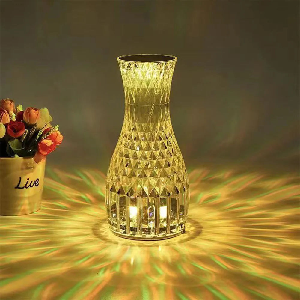 Transparent crystal vase shaped LED table lamp with remote control on a wooden bedside table.