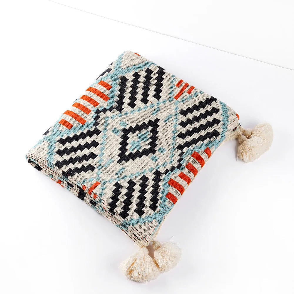 Bohemian style acrylic sofa blanket with tassel fringe in a geometric blue and pink pattern.