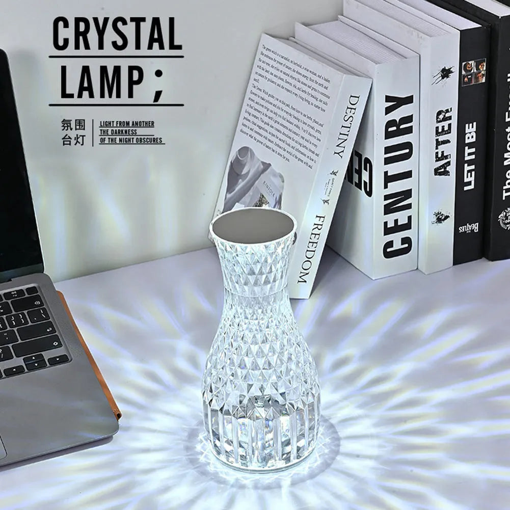 Transparent crystal vase shaped LED table lamp with remote control on a wooden bedside table.