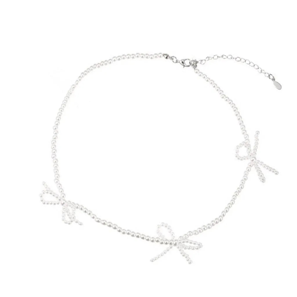 White bow-shaped imitation pearl necklace with an adjustable chain on a woman's clavicle.