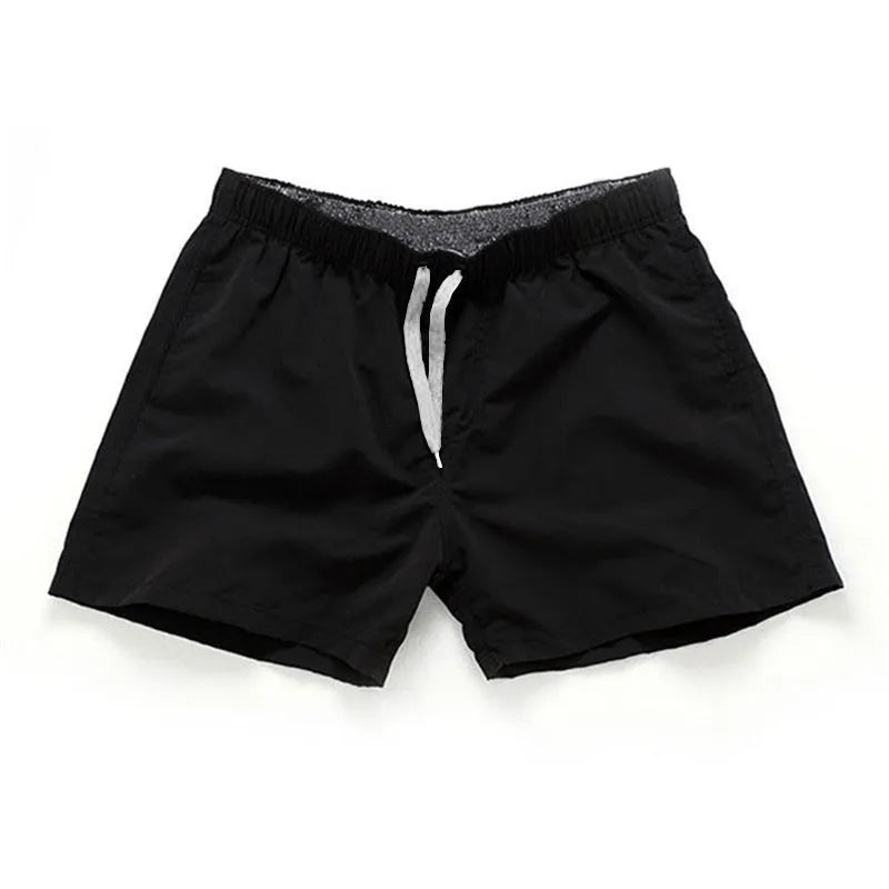 Men's straight-leg beach shorts in emerald green colour on a beach background.