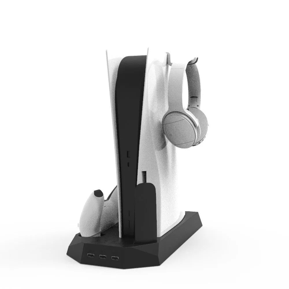 PS5 console upright on a black charging base with two controllers docked and a headset hanging