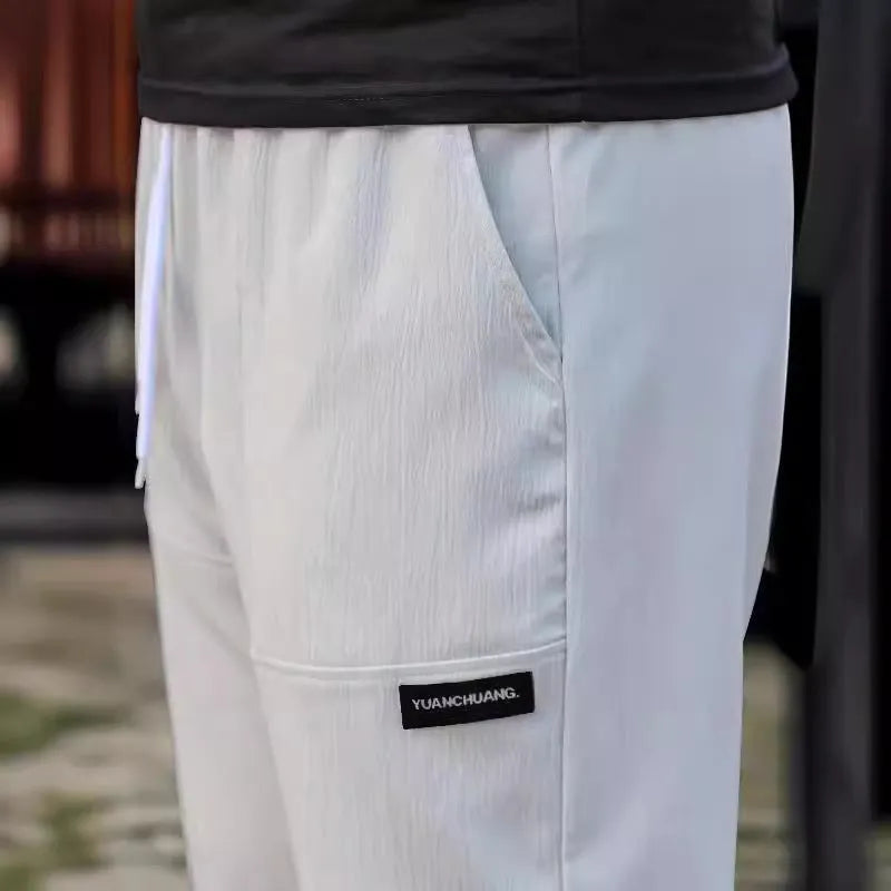 Men's light grey tapered slim-fit trousers with an elastic waistband on a hanger.