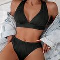 Women's black halter strap bikini with split shorts on beach background