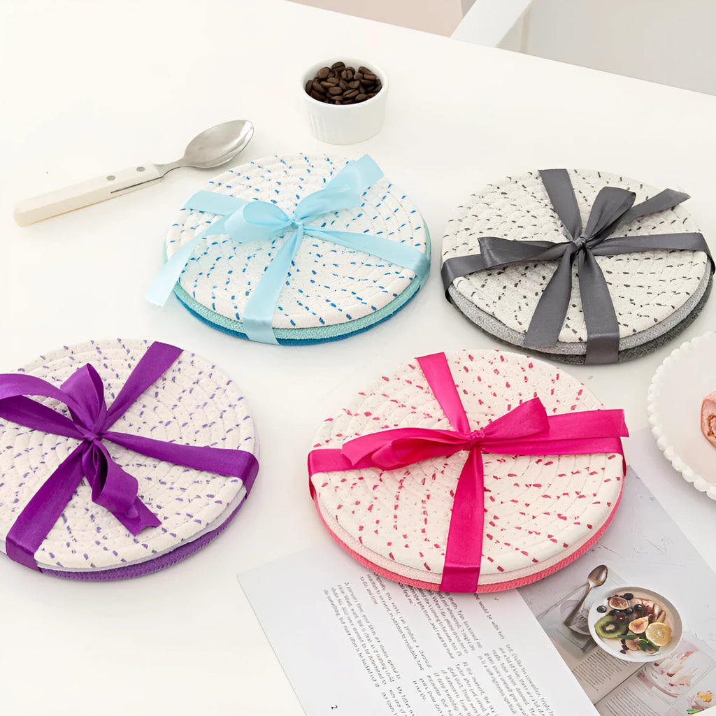 Three round grey cotton cord coasters arranged on a wooden table.