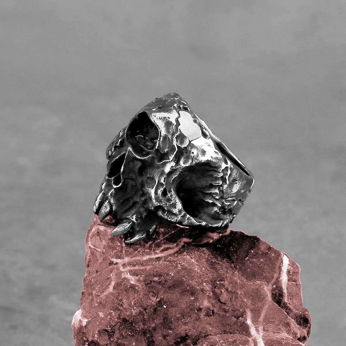 Close-up of a silver-toned alloy ring with a detailed one-eyed skull design on a black background.