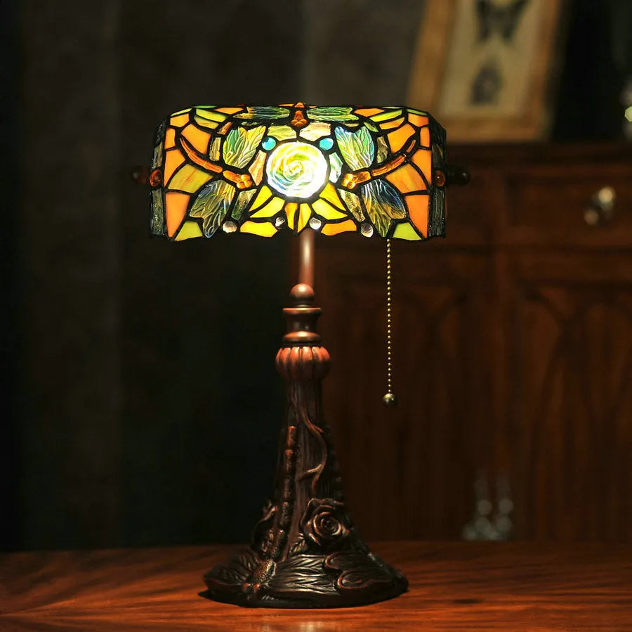 Tiffany table lamp with coloured stained glass shade and resin base on wooden desk