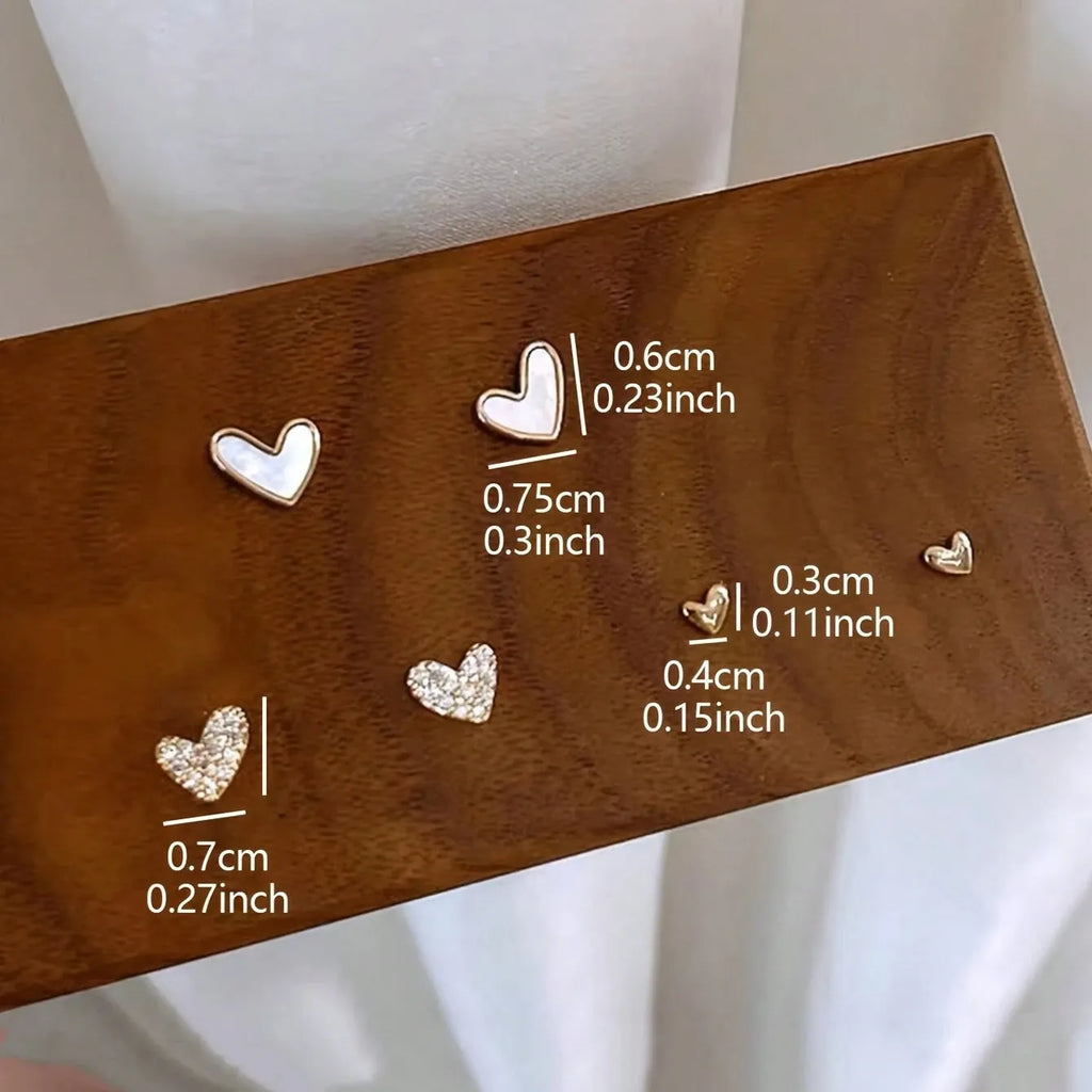 Three pairs of heart-shaped alloy earrings with electroplated finishes in gold, black, white, or pink colours.
