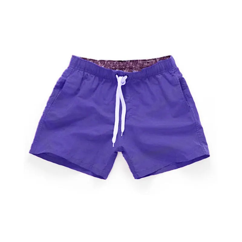 Men's straight-leg beach shorts in emerald green colour on a beach background.