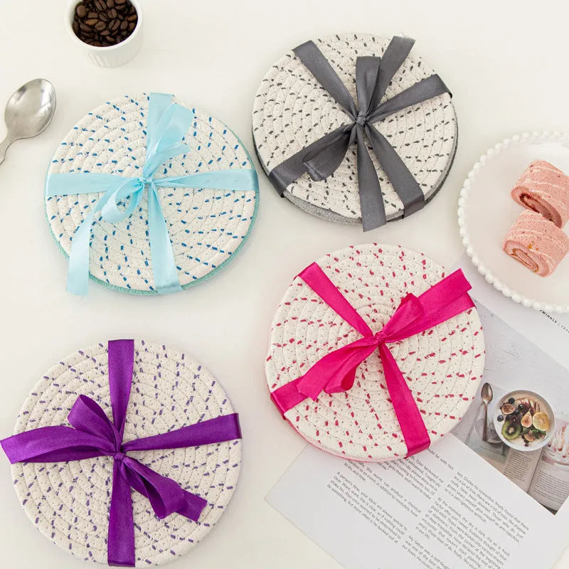 Three round grey cotton cord coasters arranged on a wooden table.