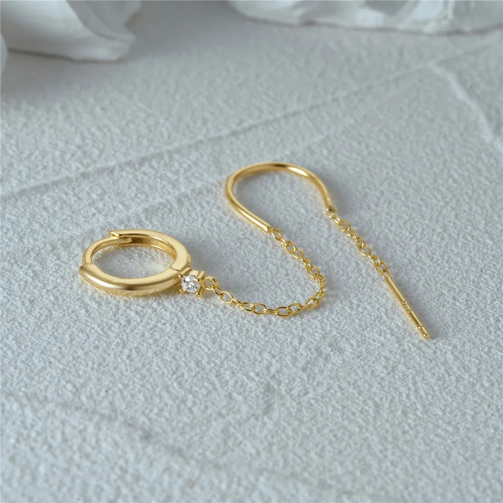 Close-up of a sterling silver stud earring with a geometric flower shape and dangling gold-tone tassel and chain details.
