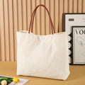 Beige white canvas tote bag with shoulder straps and front slip pockets