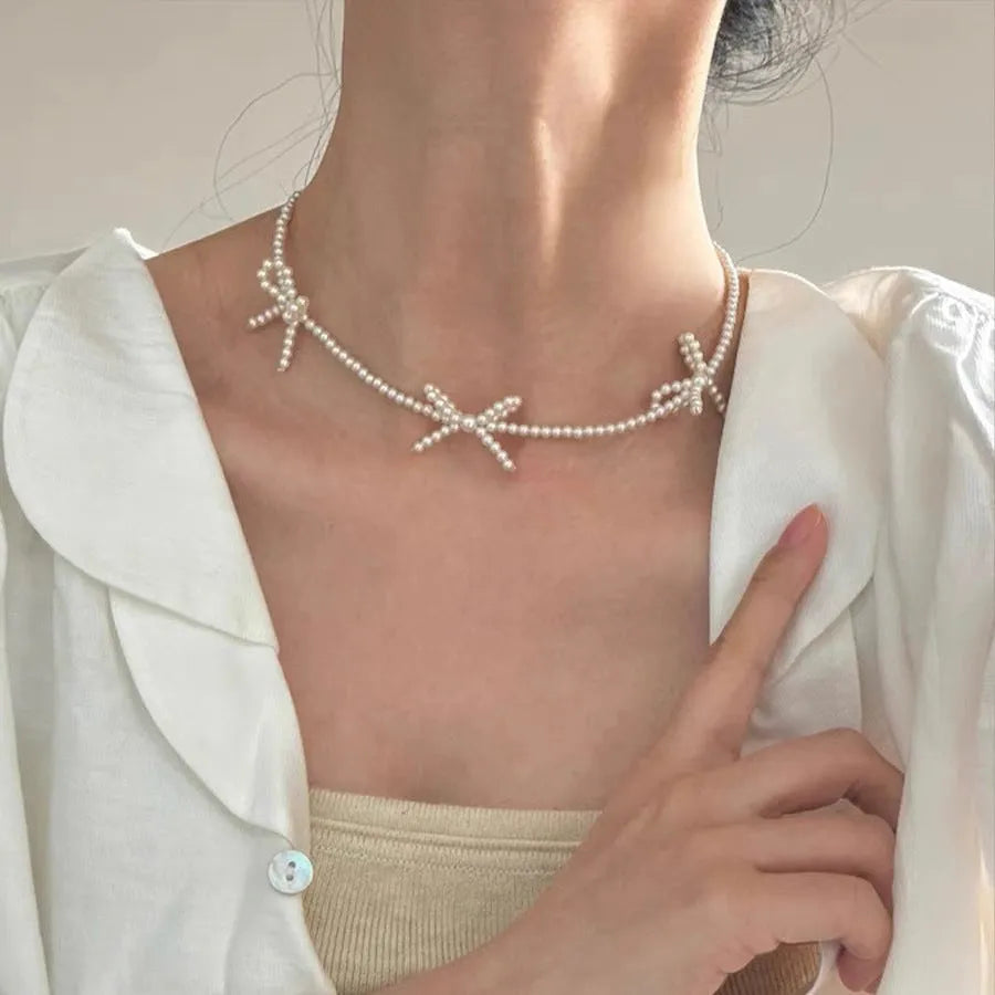 White bow-shaped imitation pearl necklace with an adjustable chain on a woman's clavicle.